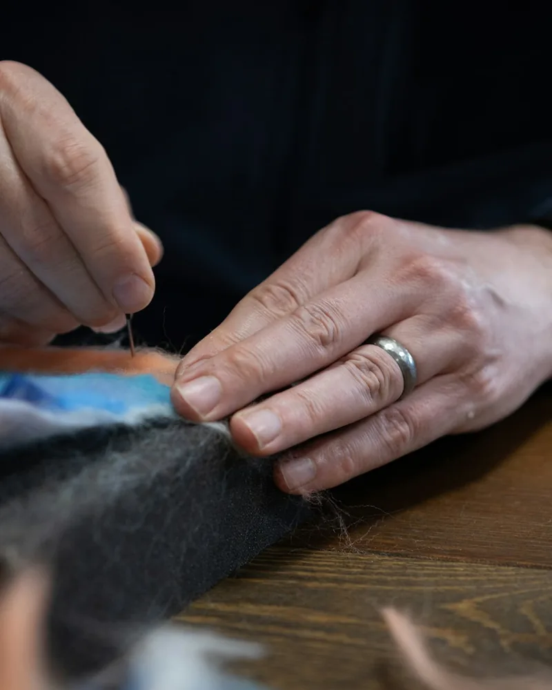 Fieltro con aguja sobre una base textil sujeta en un bastidor, con mechas de lana de colores alrededor