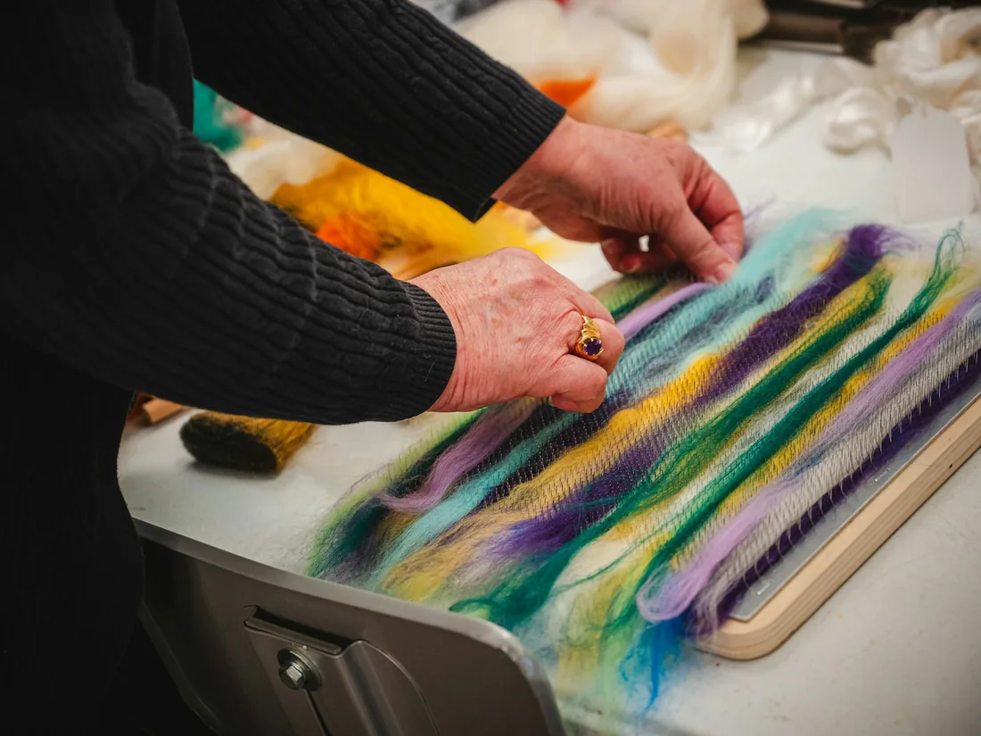 Manos separando y mezclando mechas de lana teñida sobre una mesa de trabajo